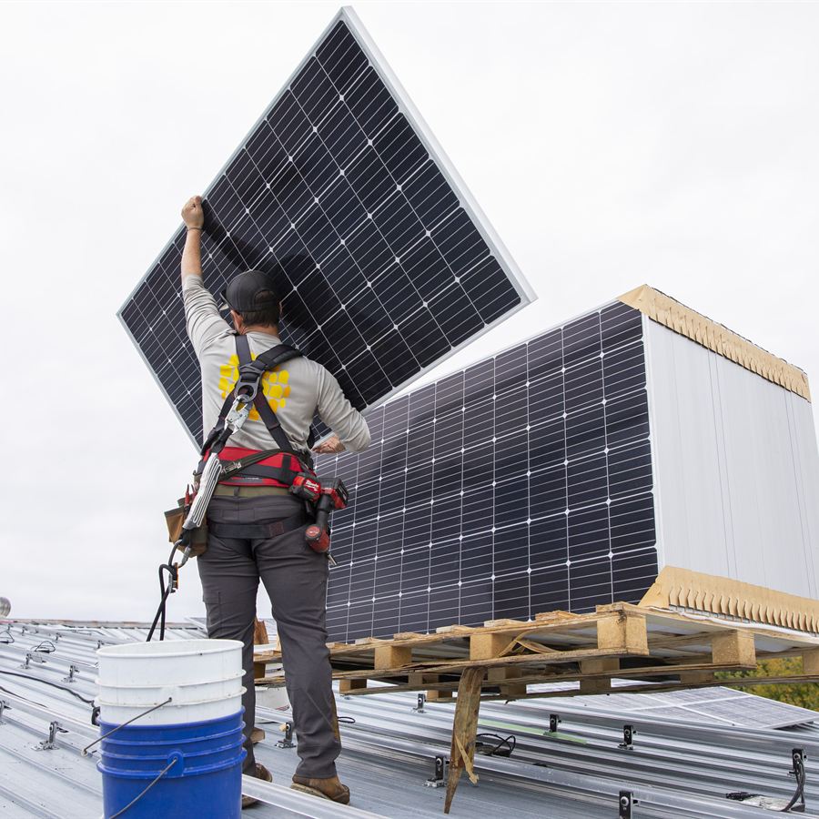 Field technician carrying a solar module on a metal roof